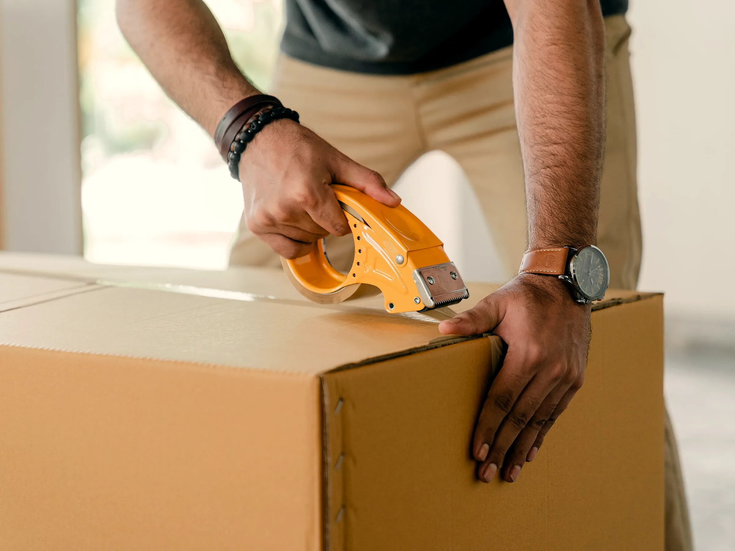 Hands sealing a corrugated carton with clear packing tape