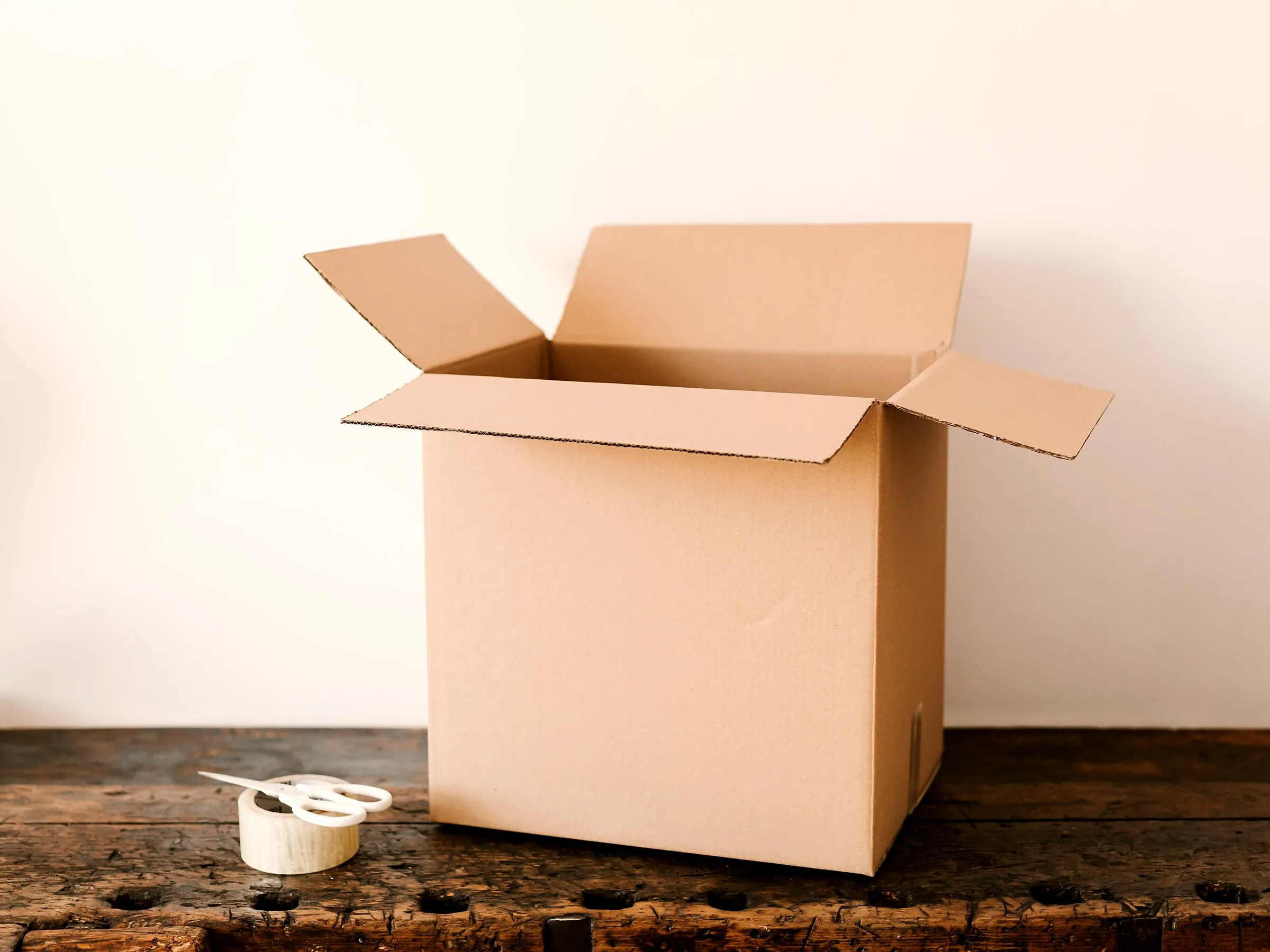 Open corrugated cardboard box with packing tape and scissors on a workbench